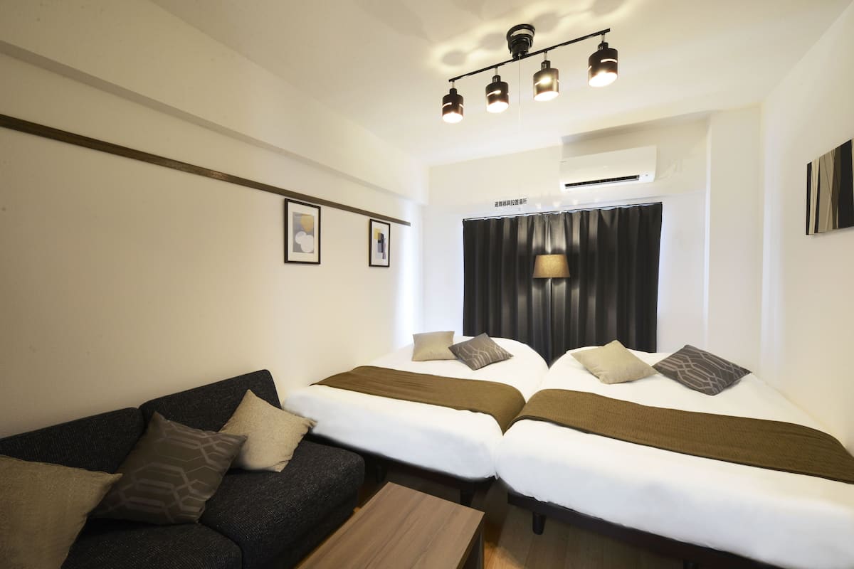 A hotel room with two beds, a sofa, a small table, and a ceiling light fixture.