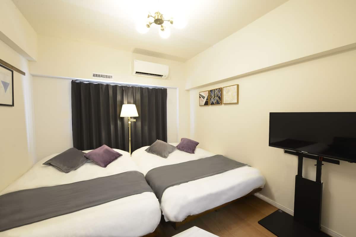A hotel room with two beds, a flat-screen TV, an air conditioning unit, and a ceiling fan.