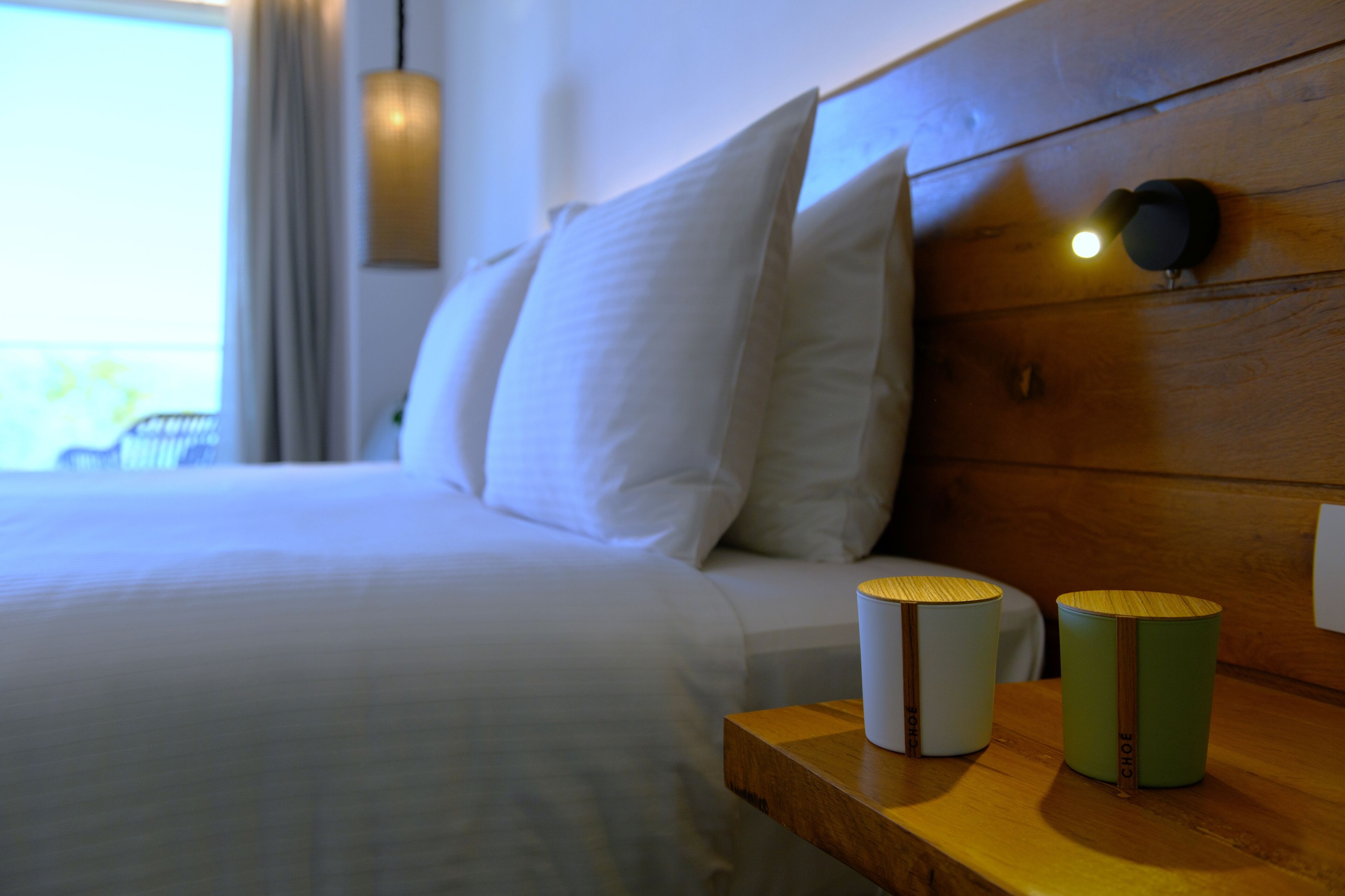 A neatly made bed with white linens, a wooden headboard, and two bedside tables with cylindrical containers.