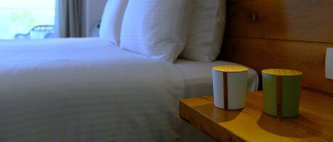 A neatly made bed with white linens, a wooden headboard, and two bedside tables with cylindrical containers.