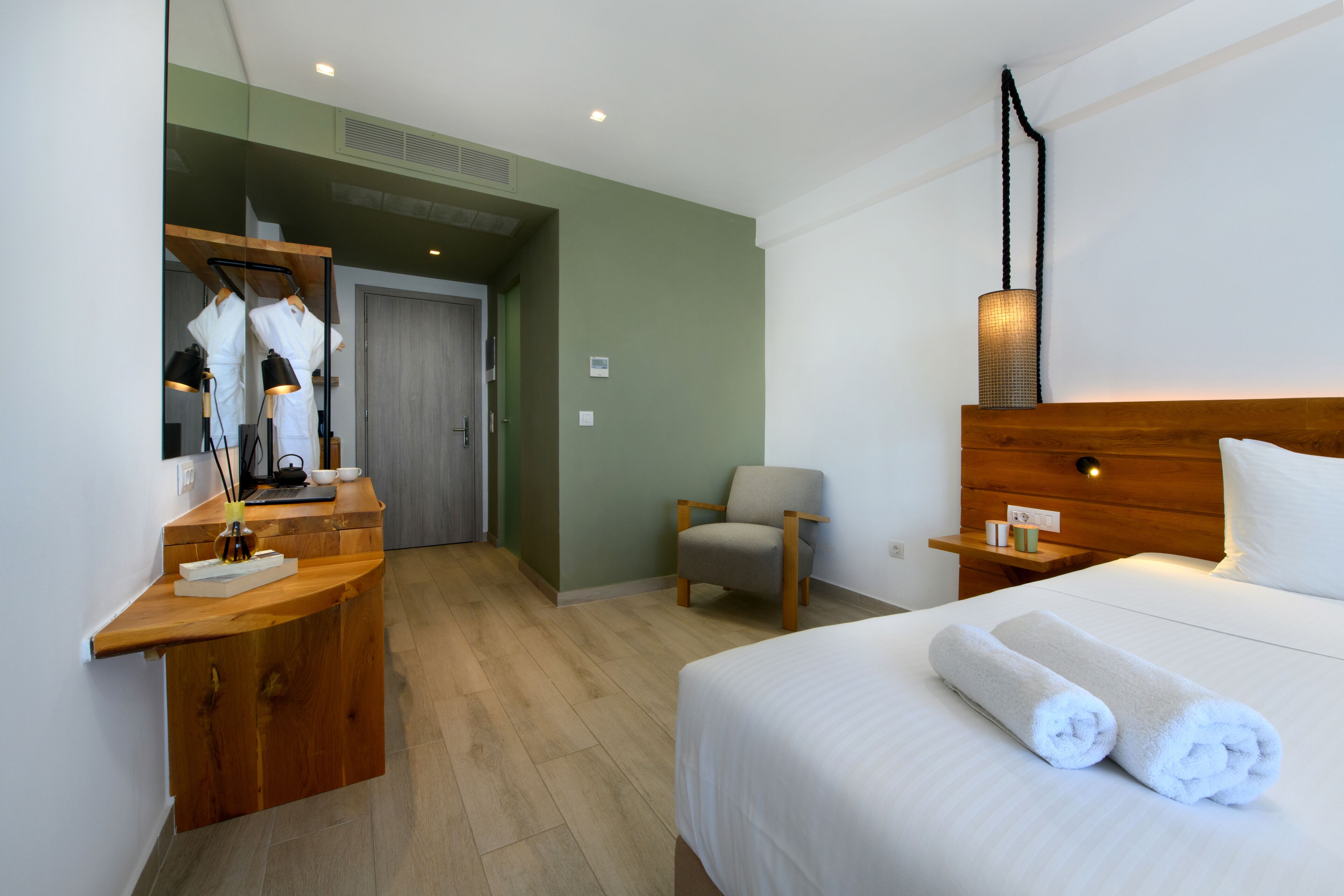 A hotel room with a wooden desk, a chair, a bed with white linens, and a nightstand with a lamp.