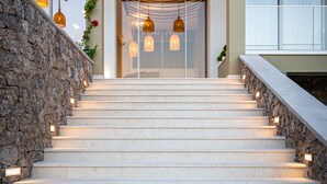 Una escalera con paredes de piedra e iluminación cálida, que lleva a la entrada de un edificio con puertas de vidrio y lámparas colgantes.