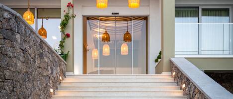 A staircase with stone walls and warm lighting, leading to a building entrance with glass doors and hanging lights.