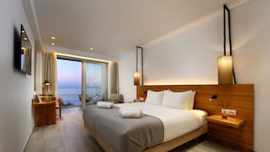 Una habitación de hotel moderna con una cama grande, una mesita de noche de madera, un escritorio con una silla y vistas al mar.