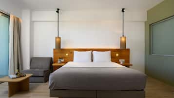 A modern hotel room with a large bed, a grey sofa, a wooden nightstand, and a wall-mounted TV.