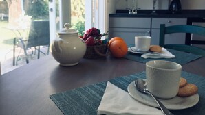 A dining table with a teapot, fruit basket, orange, and a cup.