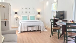 A modern bedroom with a bed, bedside lamps, a desk with a chair, a television, and a window with blinds.