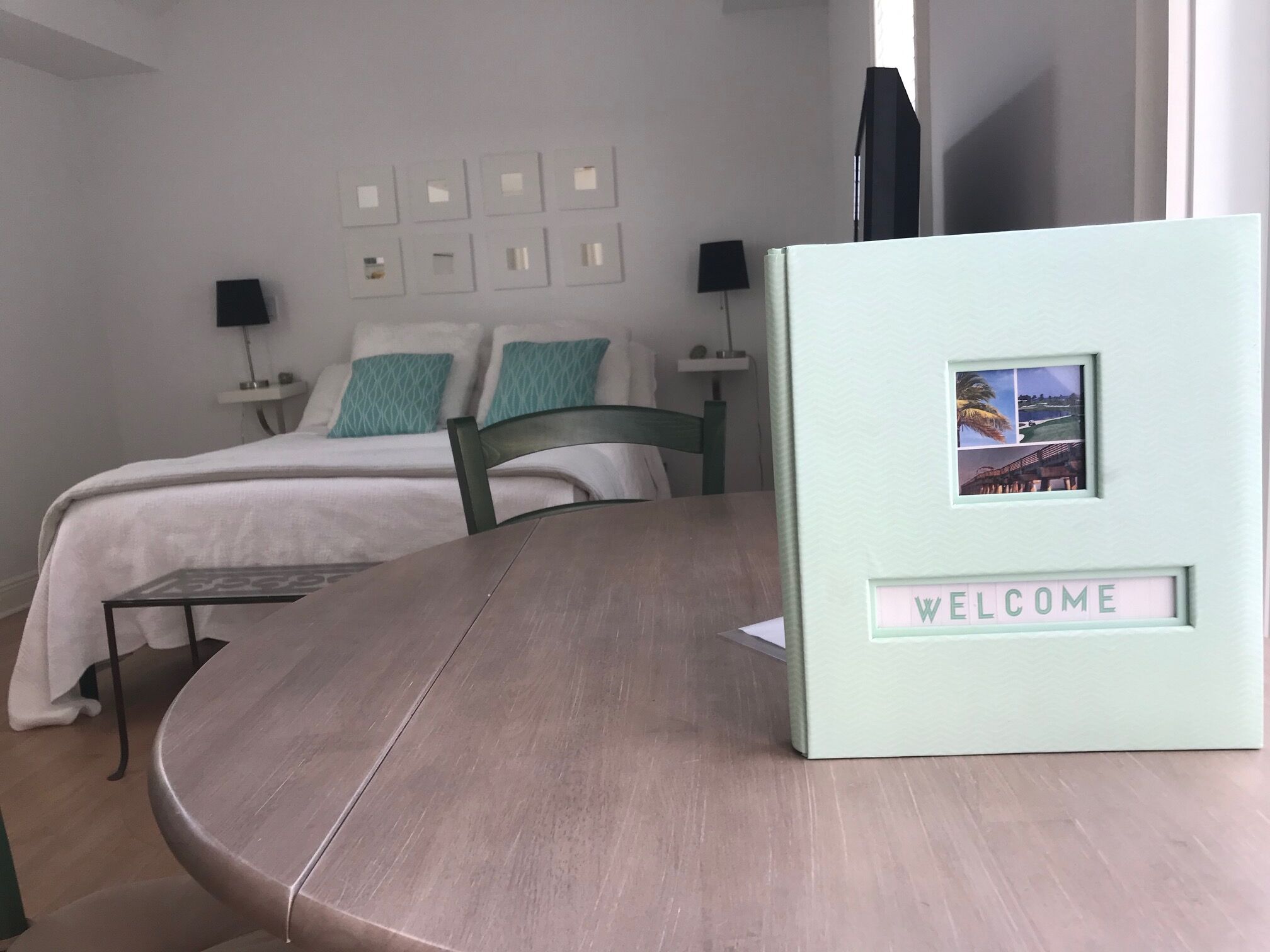 Ein Hotelzimmer mit Bett, Nachttisch, Stuhl, Tisch und einer Willkommensschild.