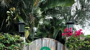 A wooden gate with a palm tree emblem, surrounded by lush greenery and a brick pathway.