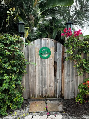 A wooden gate with a palm tree emblem, surrounded by lush greenery and a brick pathway.