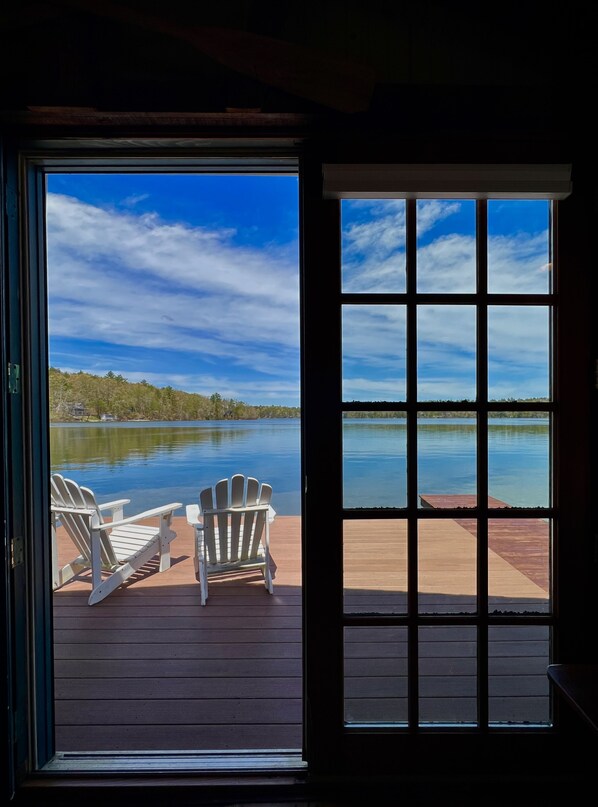 Vista desde una habitación con un ventanal grande que da a un lago y un muelle con dos sillas Adirondack.