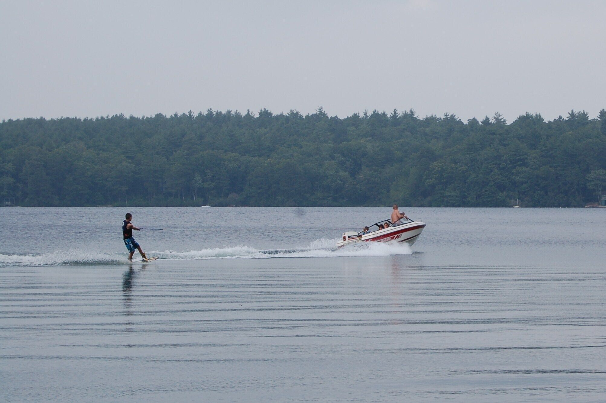A person wakeboarding on a calm lake with a boat in the background.