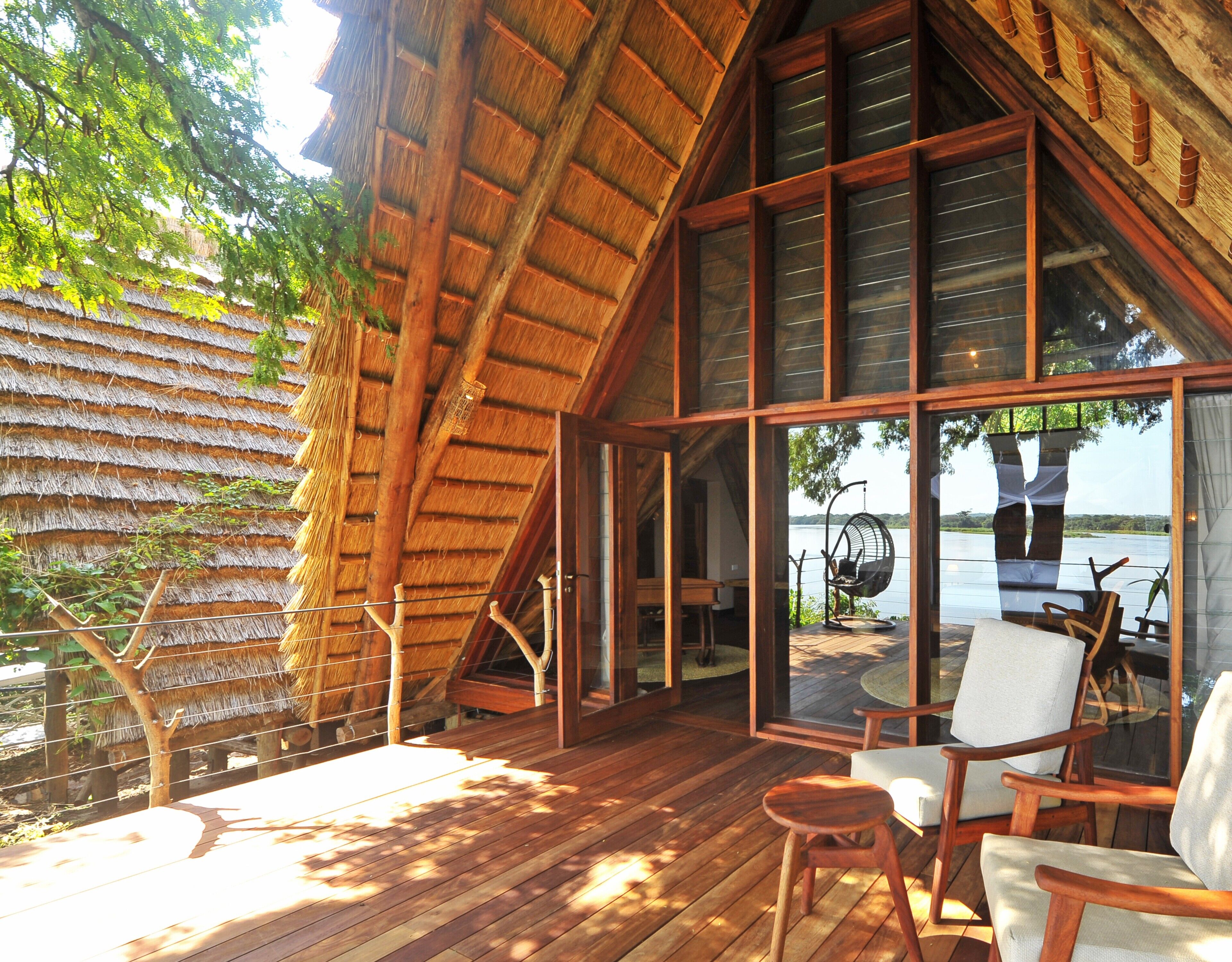 A wooden deck with a thatched roof, large windows, and a hanging chair.