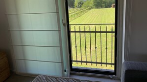 A room with a sliding glass door leading to a balcony with a view of a grassy field and mountains. - River house surrounded by greenery. (San Giacomo)