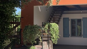 A courtyard with a stone floor, a wooden gate, and a staircase leading to a building with a white and orange facade. - River house surrounded by greenery. (San Giacomo)