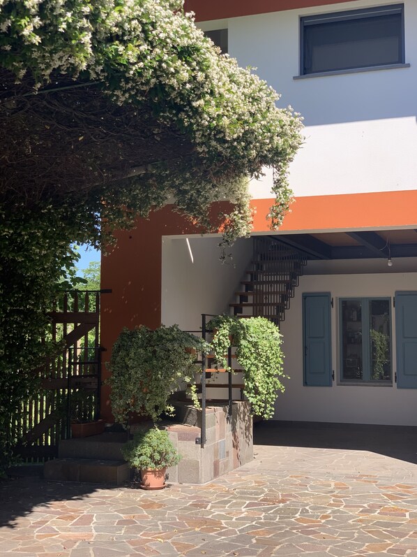 Un patio con piso de piedra, una puerta de madera y una escalera que conduce a un edificio de fachada blanca y naranja.