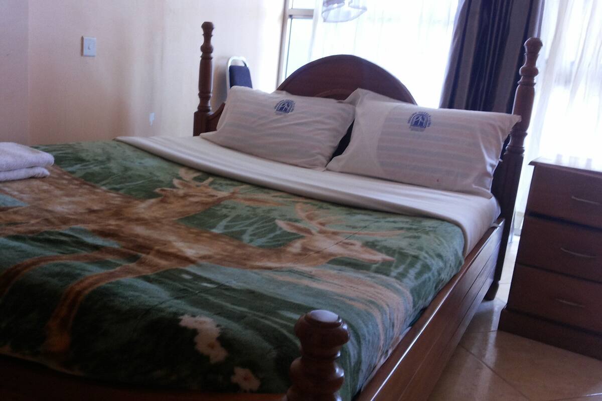 A bed with a patterned bedspread, two pillows, a wooden headboard, and a nightstand with drawers.