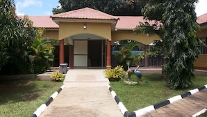 A building with a red-tiled roof, a central entrance, and a pathway leading to it. - Pauline Hotel (Lira)