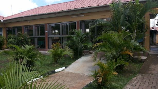 A building with a red-tiled roof, large windows, and a well-maintained garden with palm trees and a concrete pathway. - Pauline Hotel (Lira)