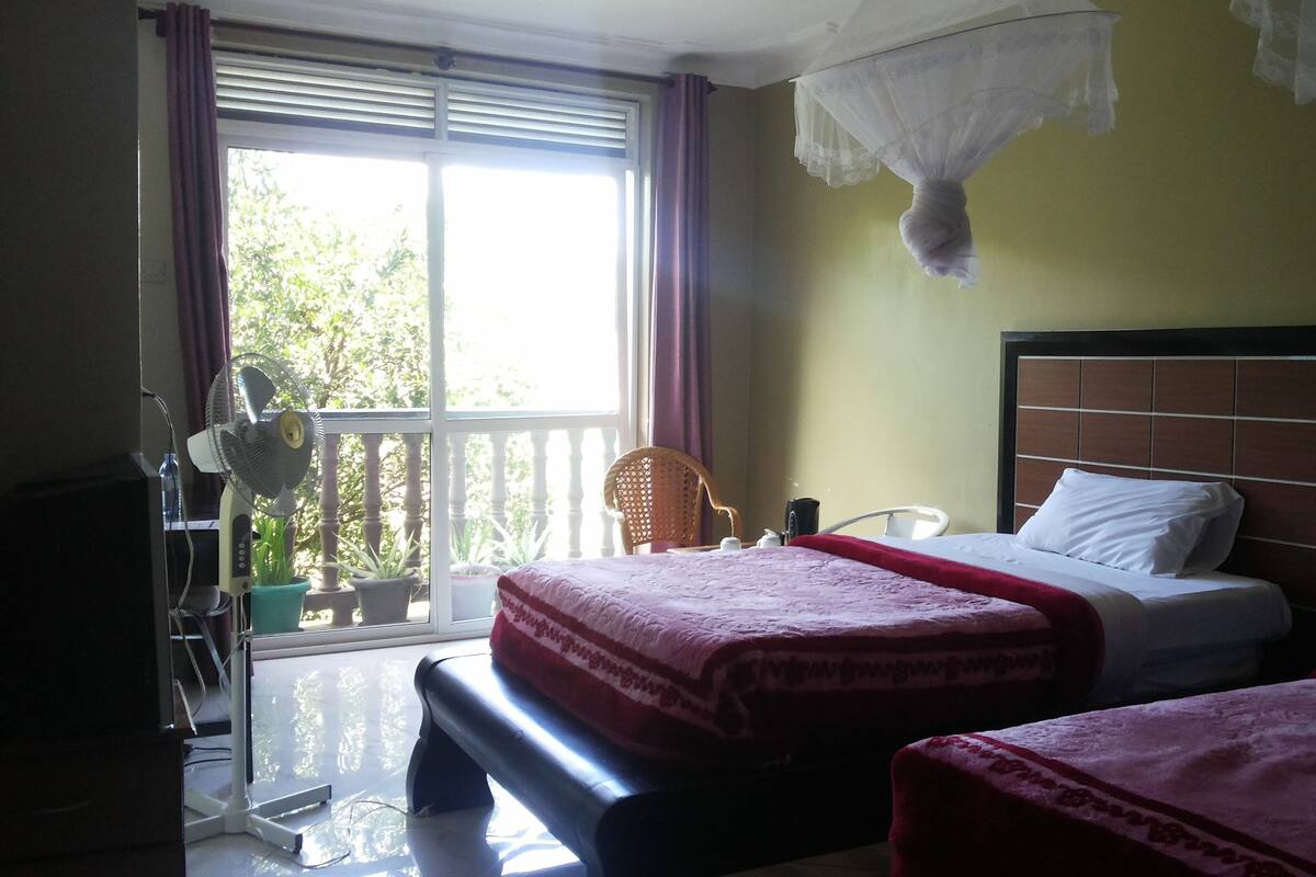 A hotel room with a balcony, a bed with a headboard, a chair, and a desk with a lamp.