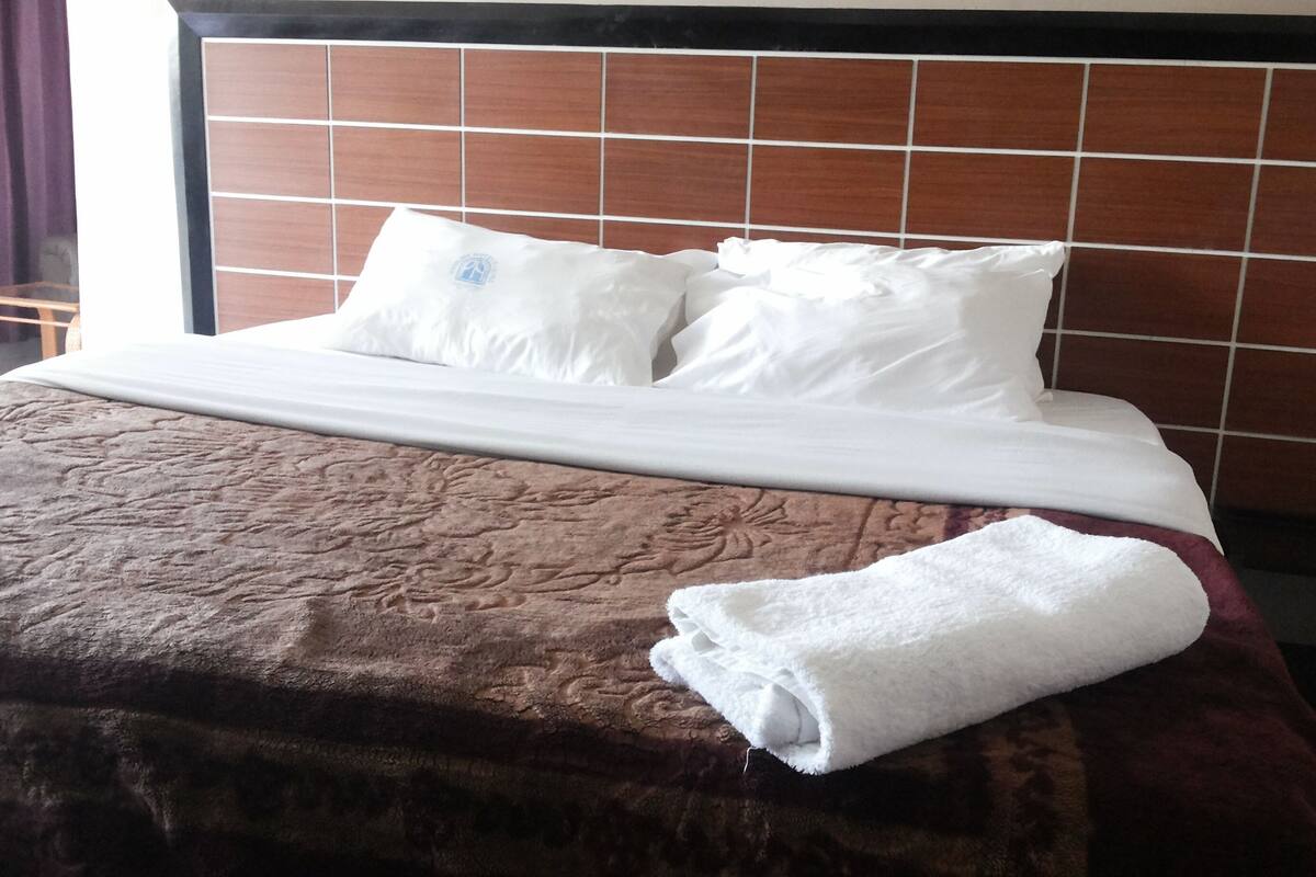 A neatly made bed with a brown bedspread, white pillows, and a folded white towel.