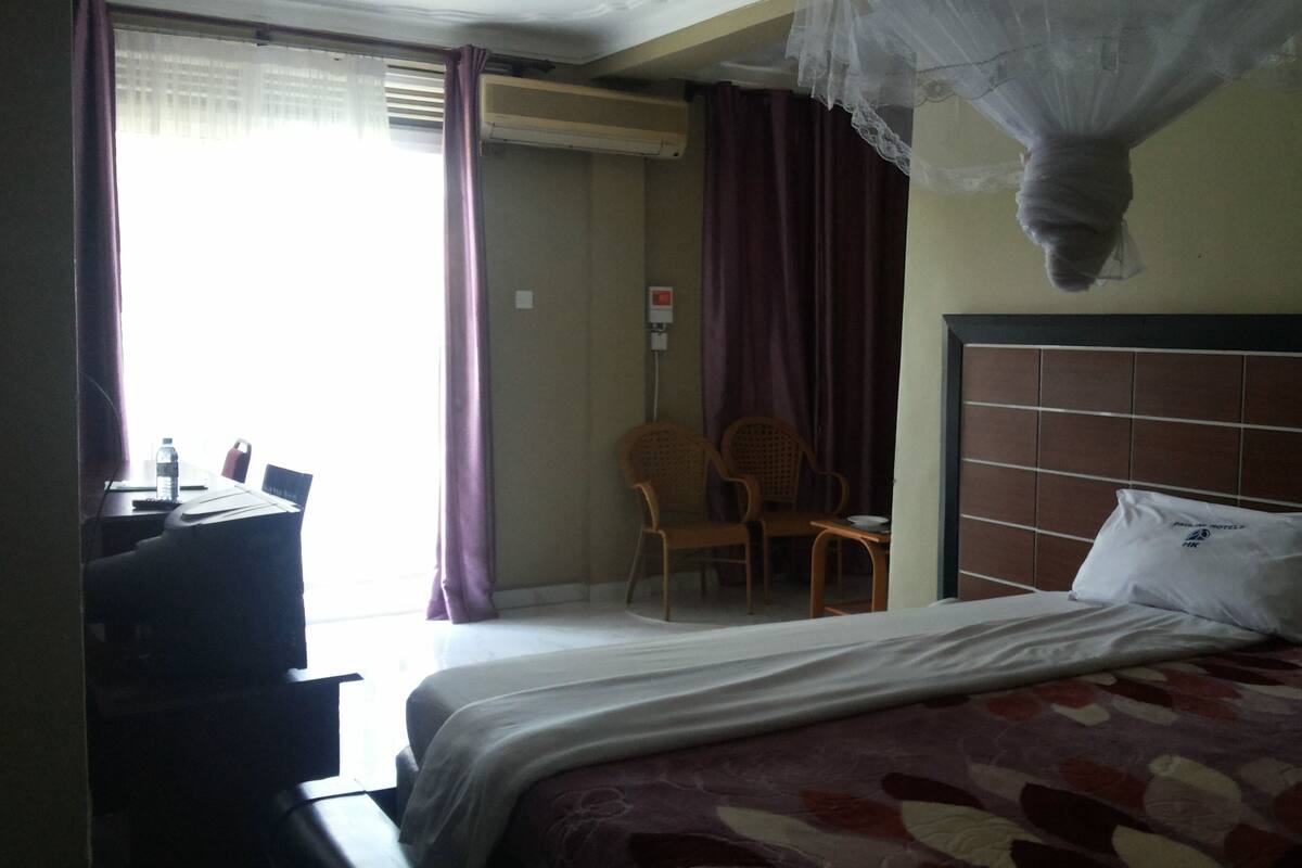 A hotel room with a bed, a desk, a chair, and a window with curtains.