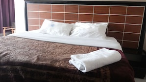 A neatly made bed with a brown bedspread and white pillows, a wooden headboard, and a folded white towel on the side. - Pauline Hotel (Lira)