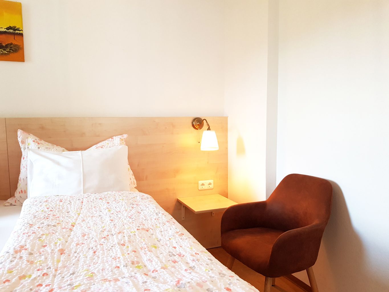 Una habitación de hotel con una cama, una mesita de noche, una lámpara y una silla.