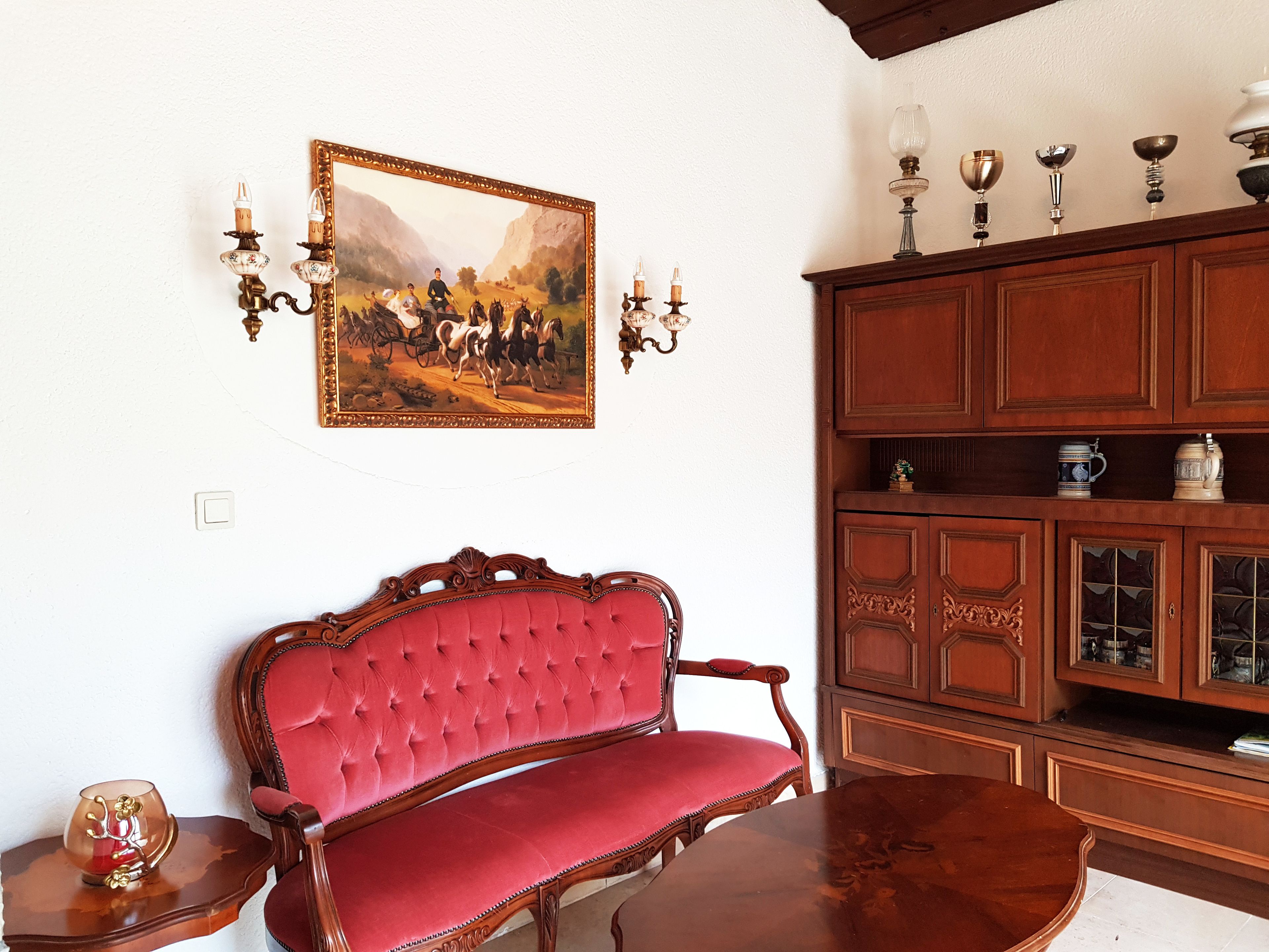 Una habitación con un sofá tapizado rojo, un mueble de madera con puertas de cristal y un cuadro en la pared.