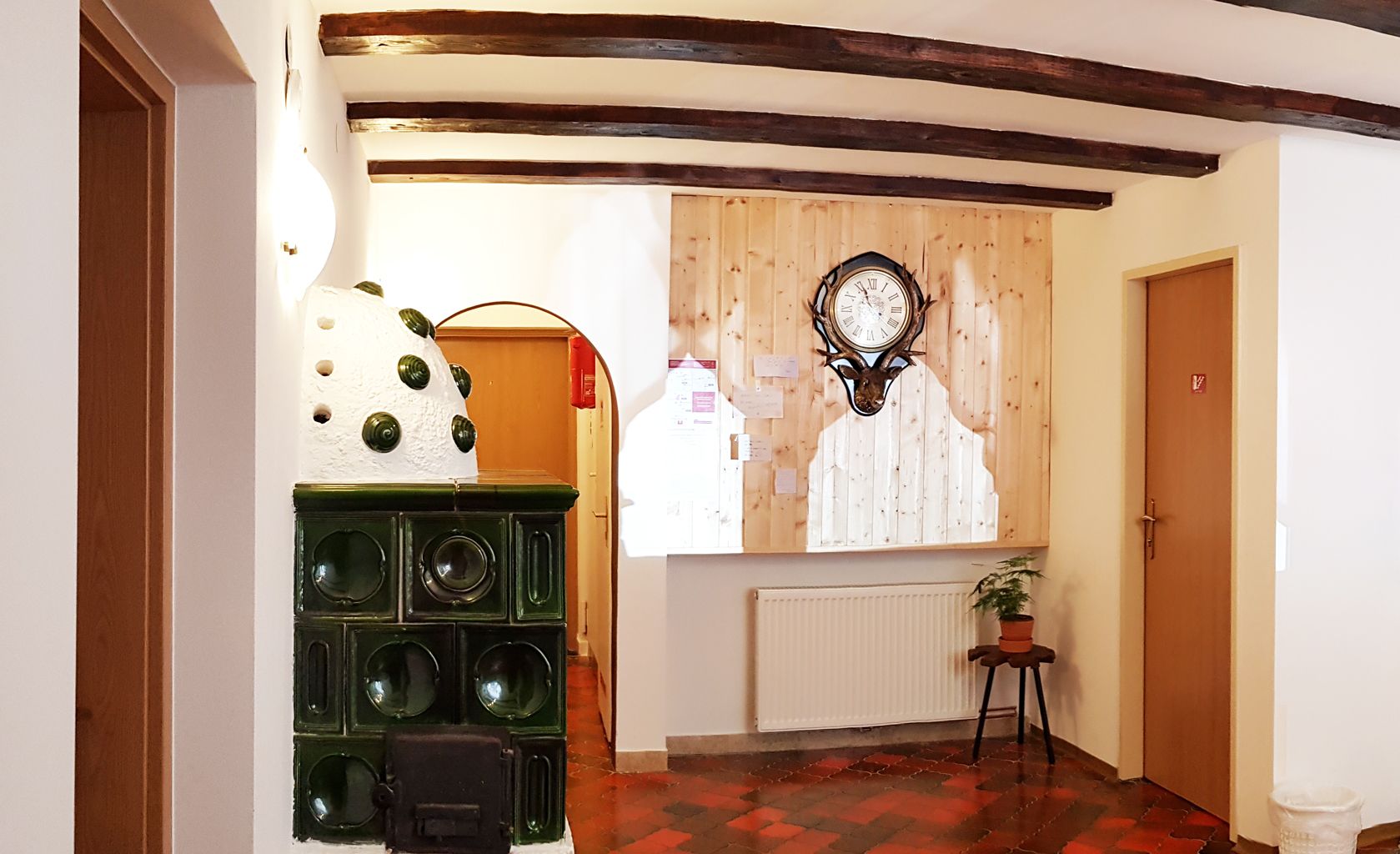 A hallway with a wooden ceiling, a clock on the wall, a radiator, and a door.