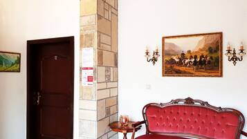 Una habitación con puerta de madera, un banco tapizado en rojo, una mesita con una vela y un cuadro en la pared.
