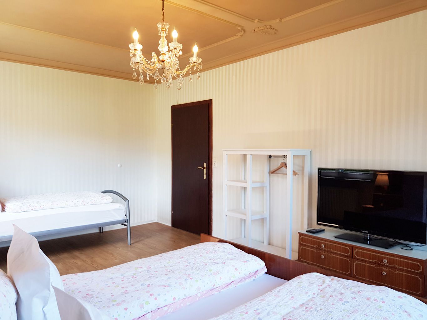 Ein Schlafzimmer mit zwei Betten, einem Kleiderschrank, einem Fernseher und einer Chandelier.