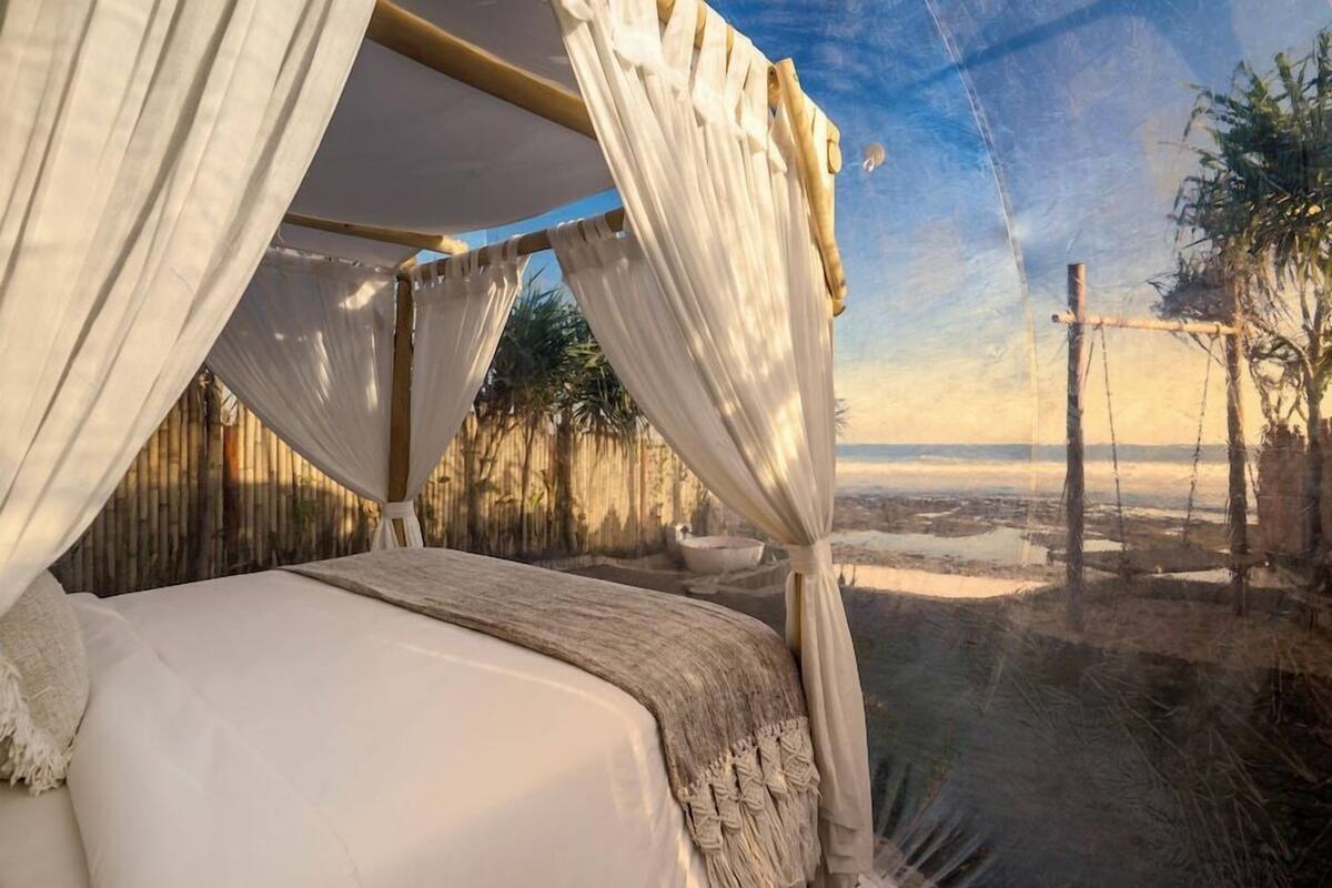 Un lit à baldaquin, une vue sur la plage et une clôture en bambou.