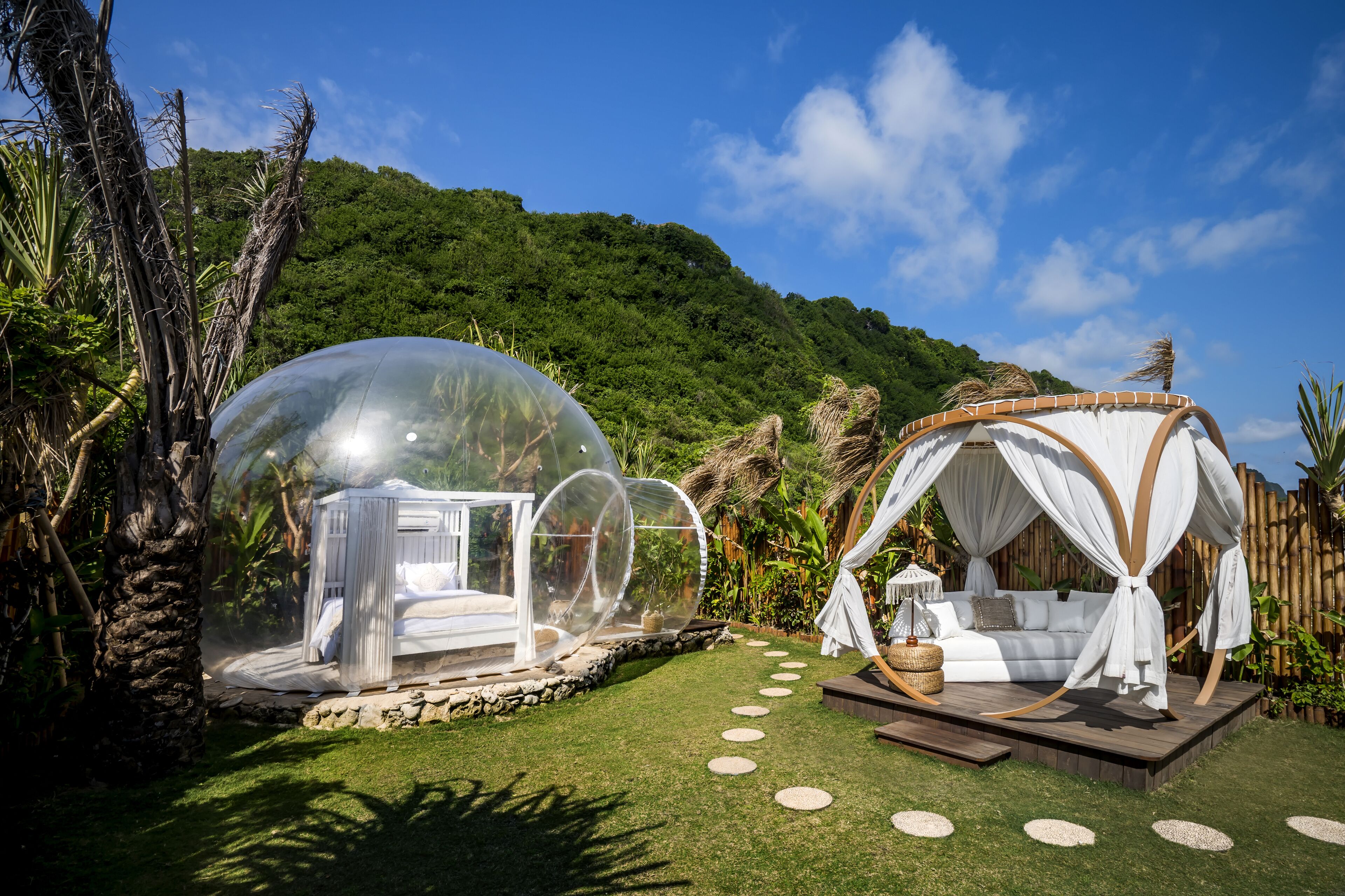 A transparent dome structure with a bed inside, a white canopy bed, and a stone pathway.