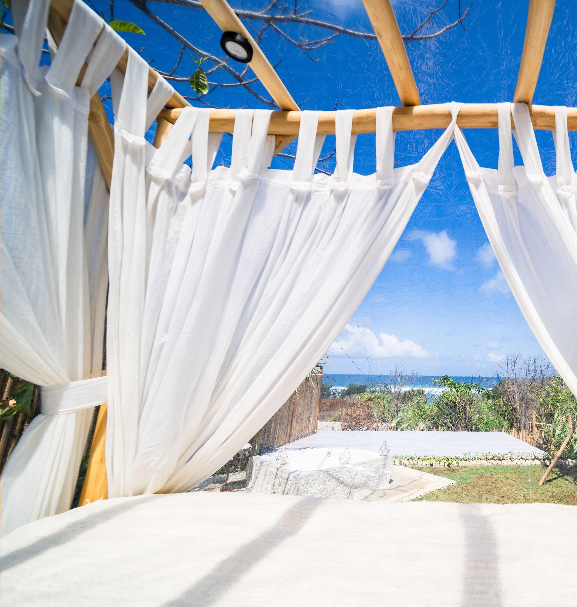 Une chambre avec vue sur l’océan, dotée d’un plafond en bois et de rideaux blancs.