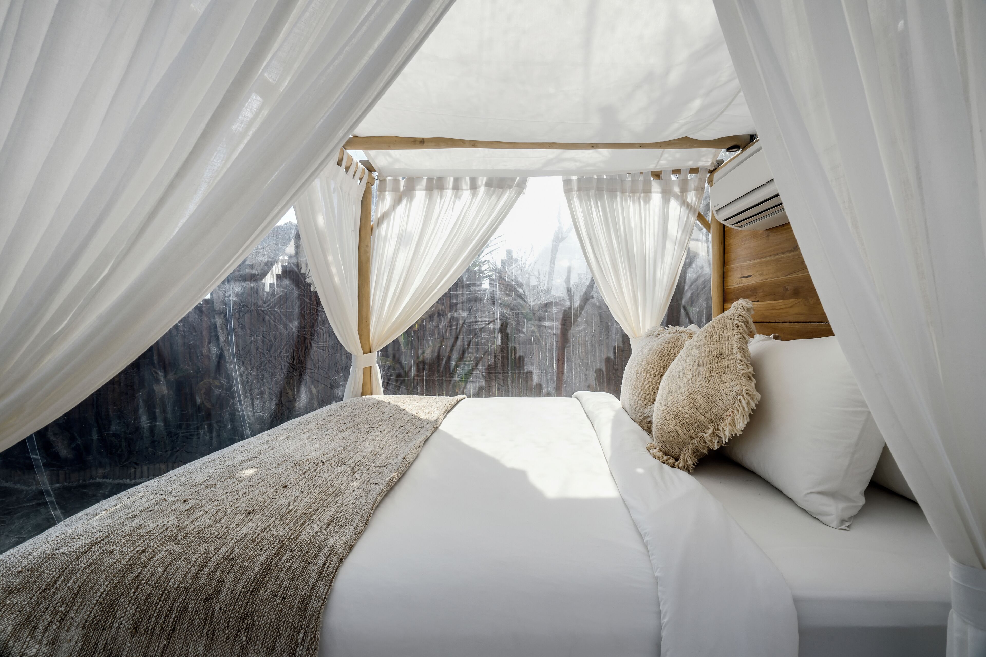 Une chambre à coucher avec un lit à baldaquin, du linge de lit blanc et une vue sur une zone boisée.