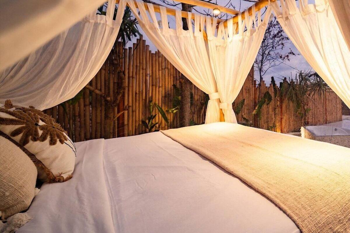 Un lit avec du linge de lit blanc, un cadre en bois et un baldaquin.