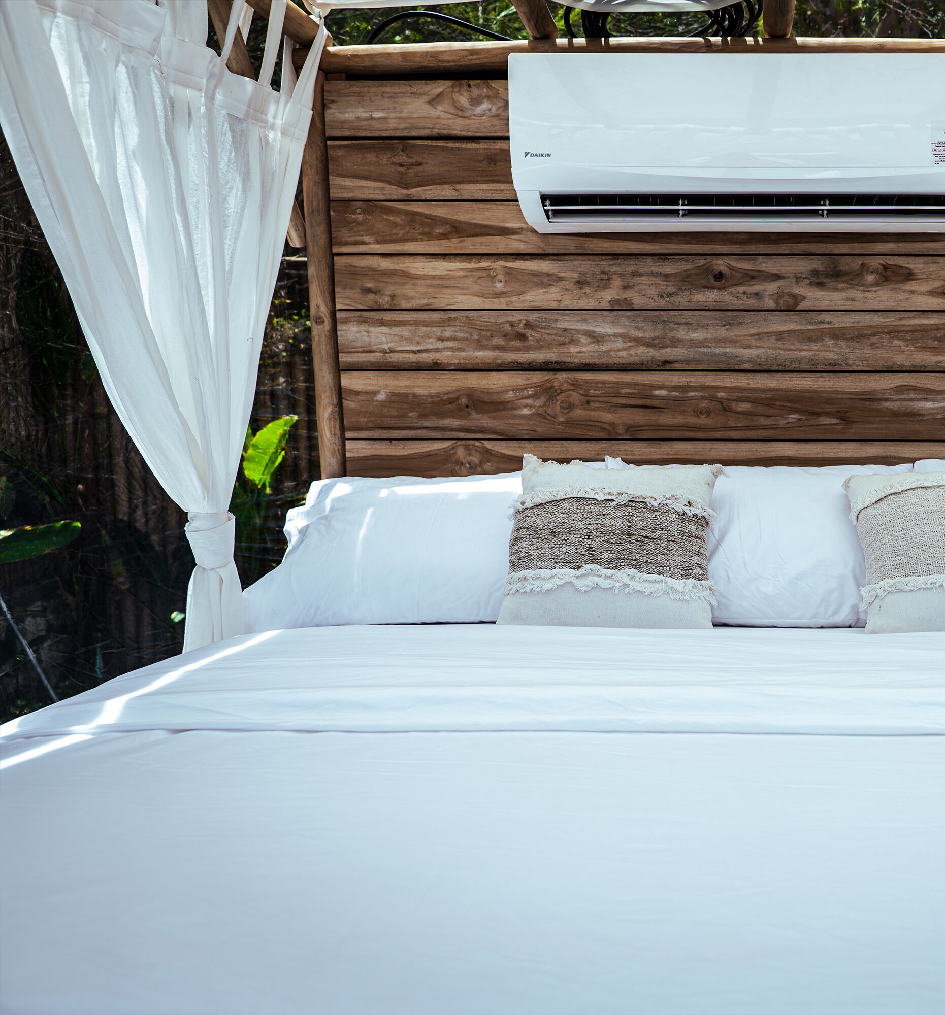A bed with white linens, a wooden headboard, and a white canopy.