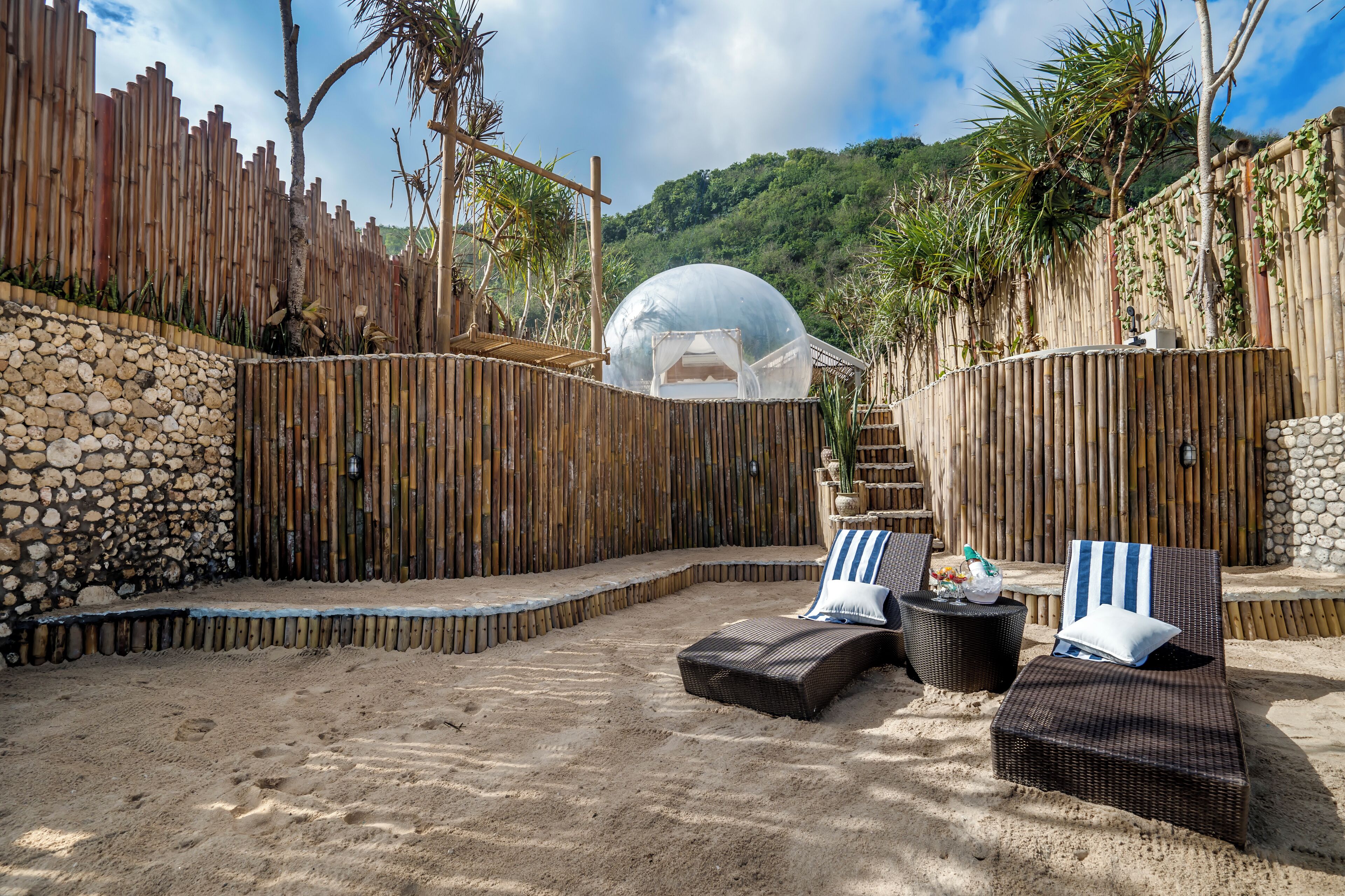 A sandy outdoor area with two wicker lounge chairs and a transparent dome structure.