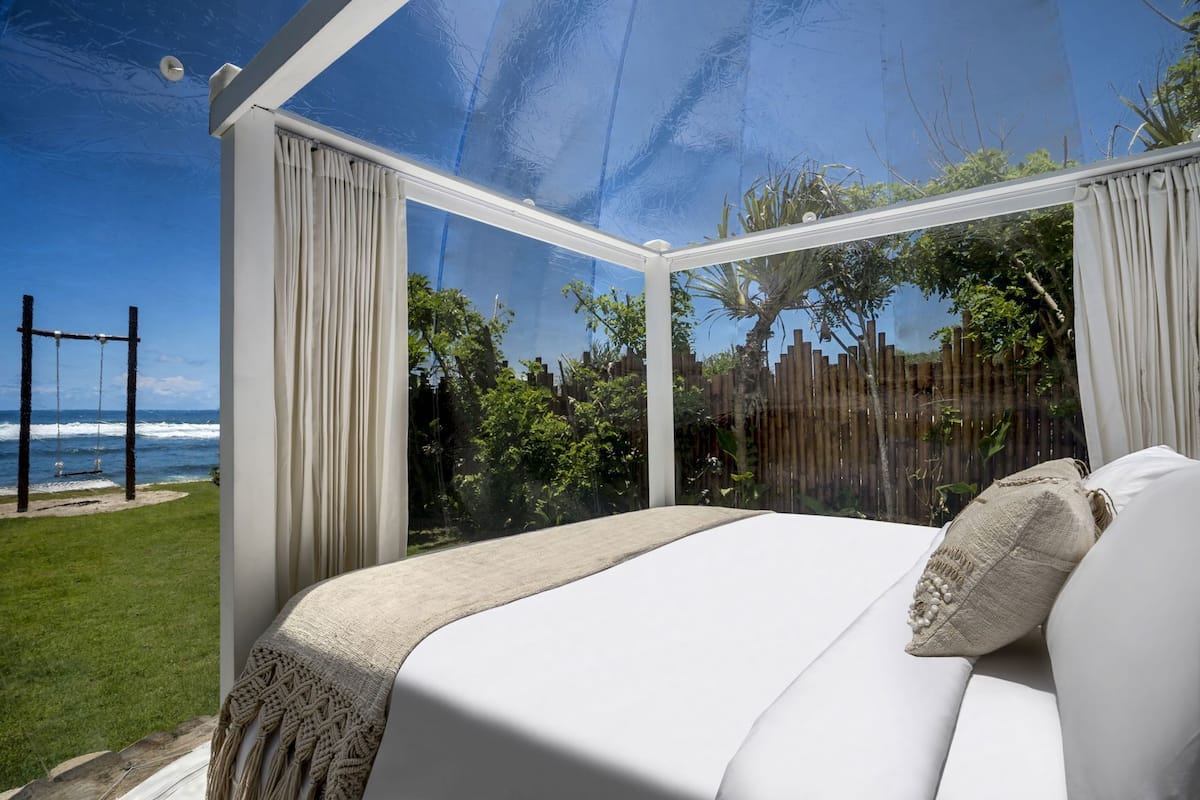 Une chambre avec une grande fenêtre en verre, un lit et une vue sur l’océan.