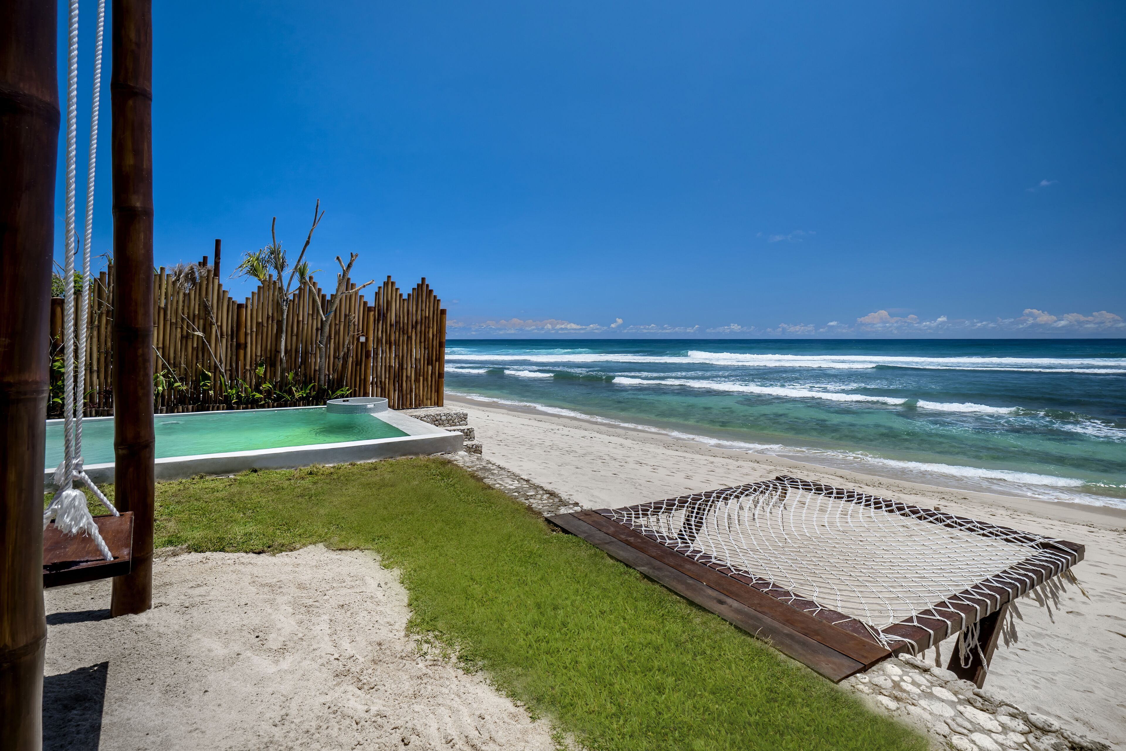 Una playa con una hamaca, una terraza de madera y una piscina.