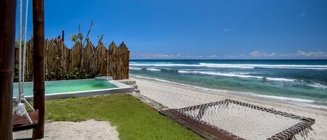 Una playa con una hamaca, una terraza de madera y una piscina.