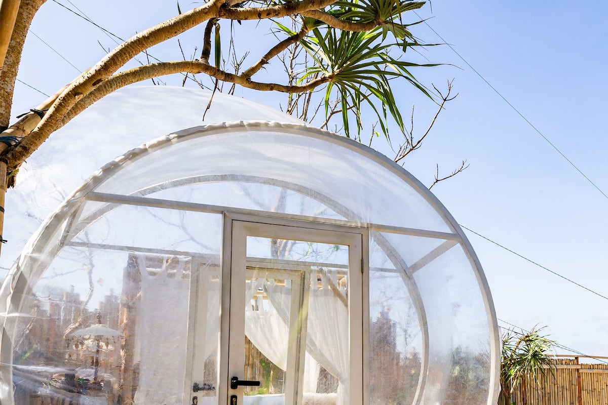 Une structure sphérique en verre dotée d’une porte coulissante, entourée d’un sentier en pierre et de verdure.