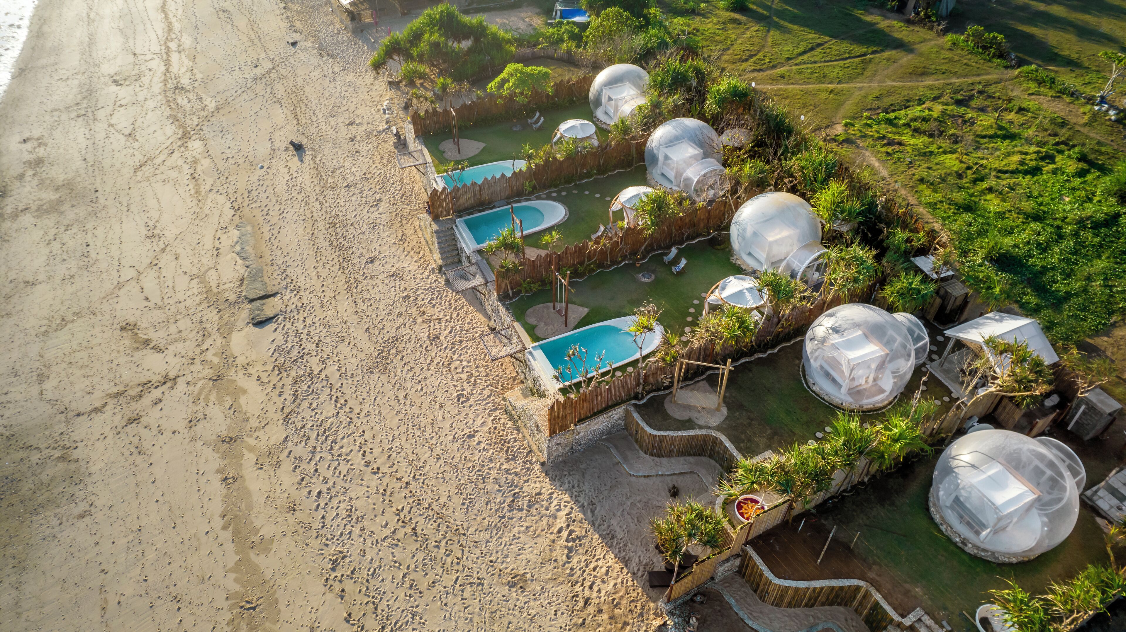 An aerial view of a beach resort with multiple dome-shaped structures, a swimming pool, and lush greenery.