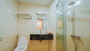 Un baño con inodoro, lavamanos, espejo y ducha con mampara de vidrio.