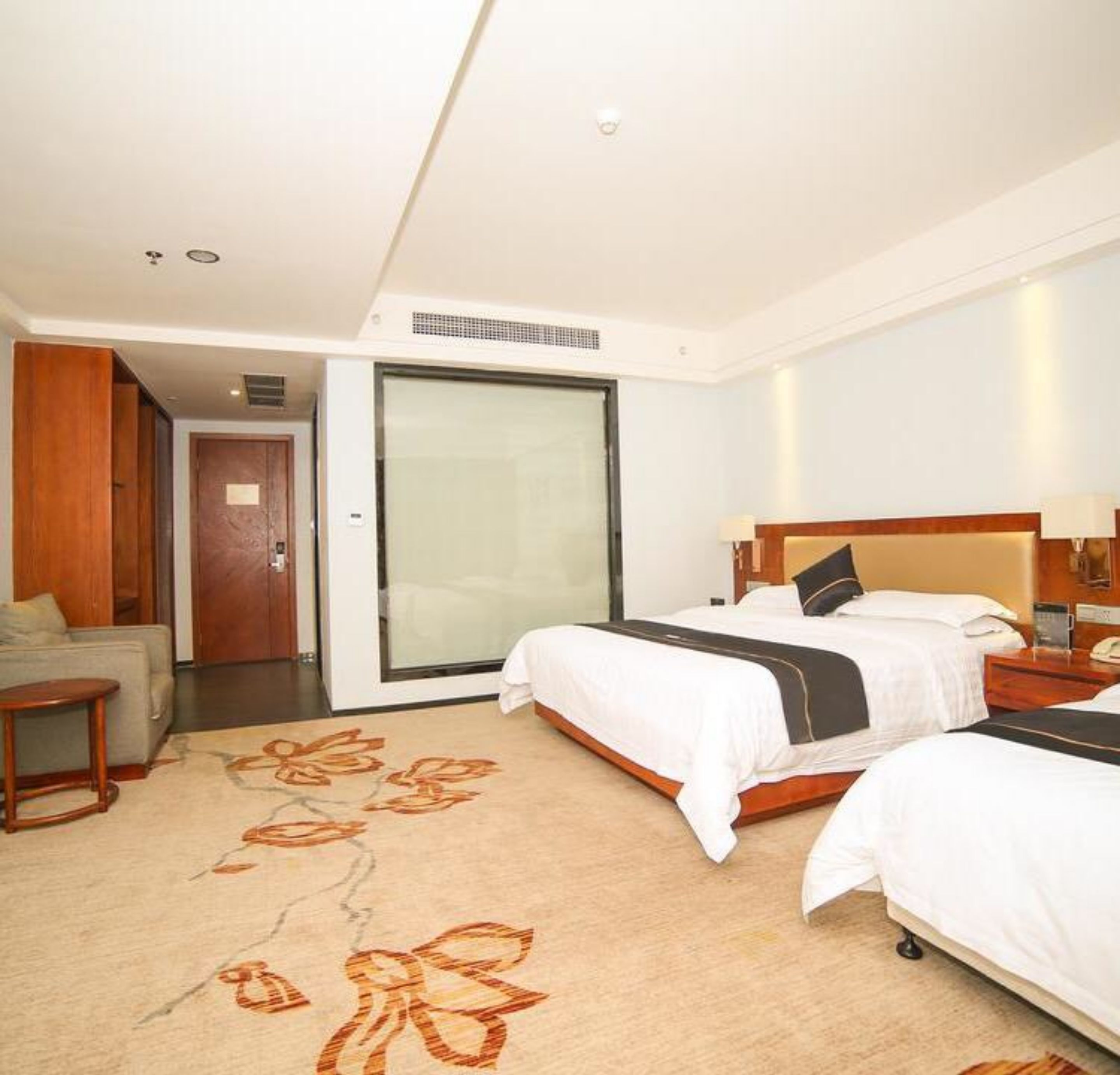 A hotel room with two beds, a sofa, a desk, and a sliding glass door to the outside.