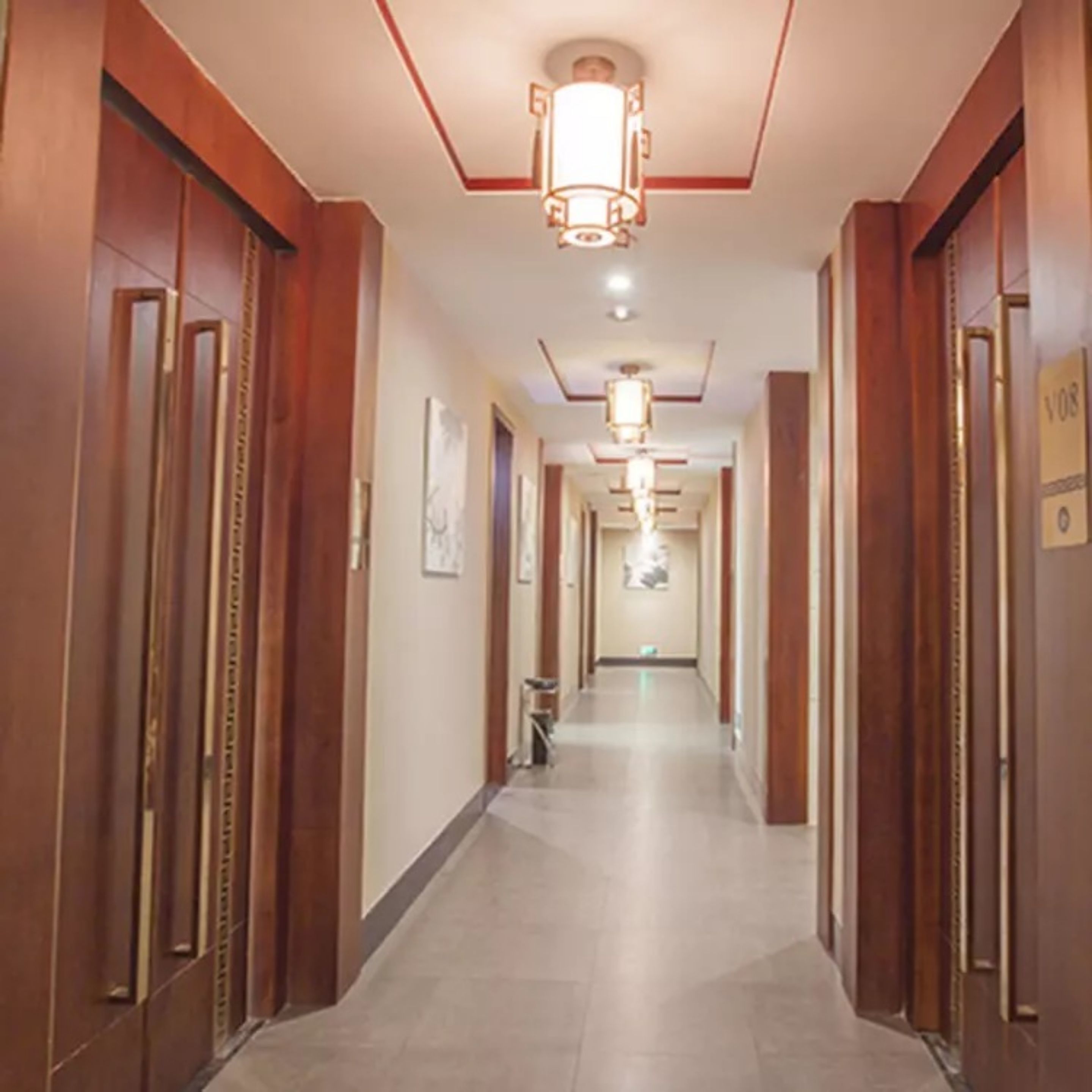 Een hotelgang met houten deuren, een betegelde vloer en een centraal hanglamp.