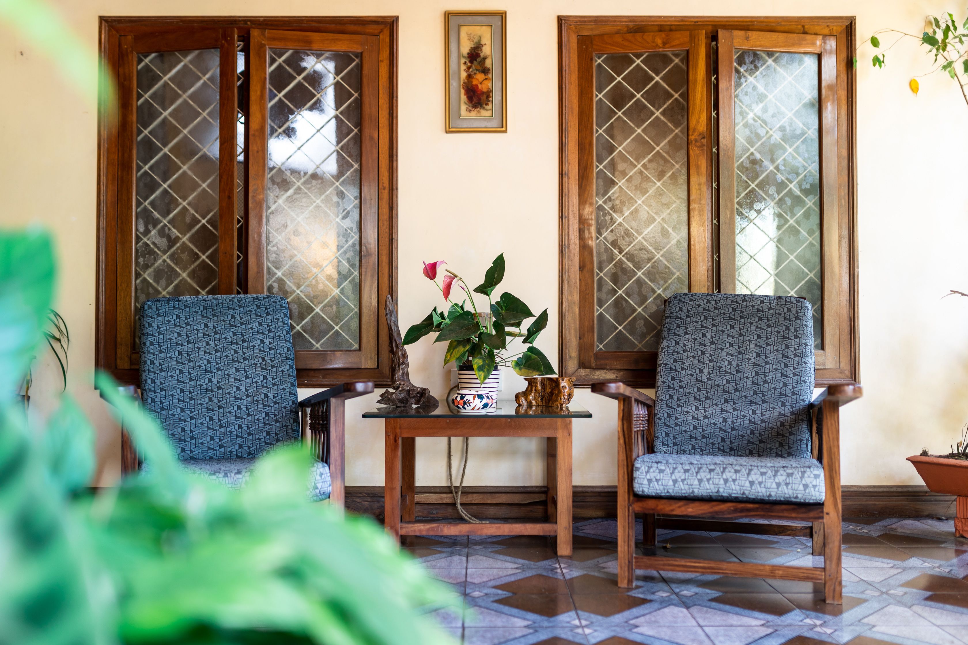 Two chairs with patterned upholstery, a small table with a vase of flowers, and a potted plant.