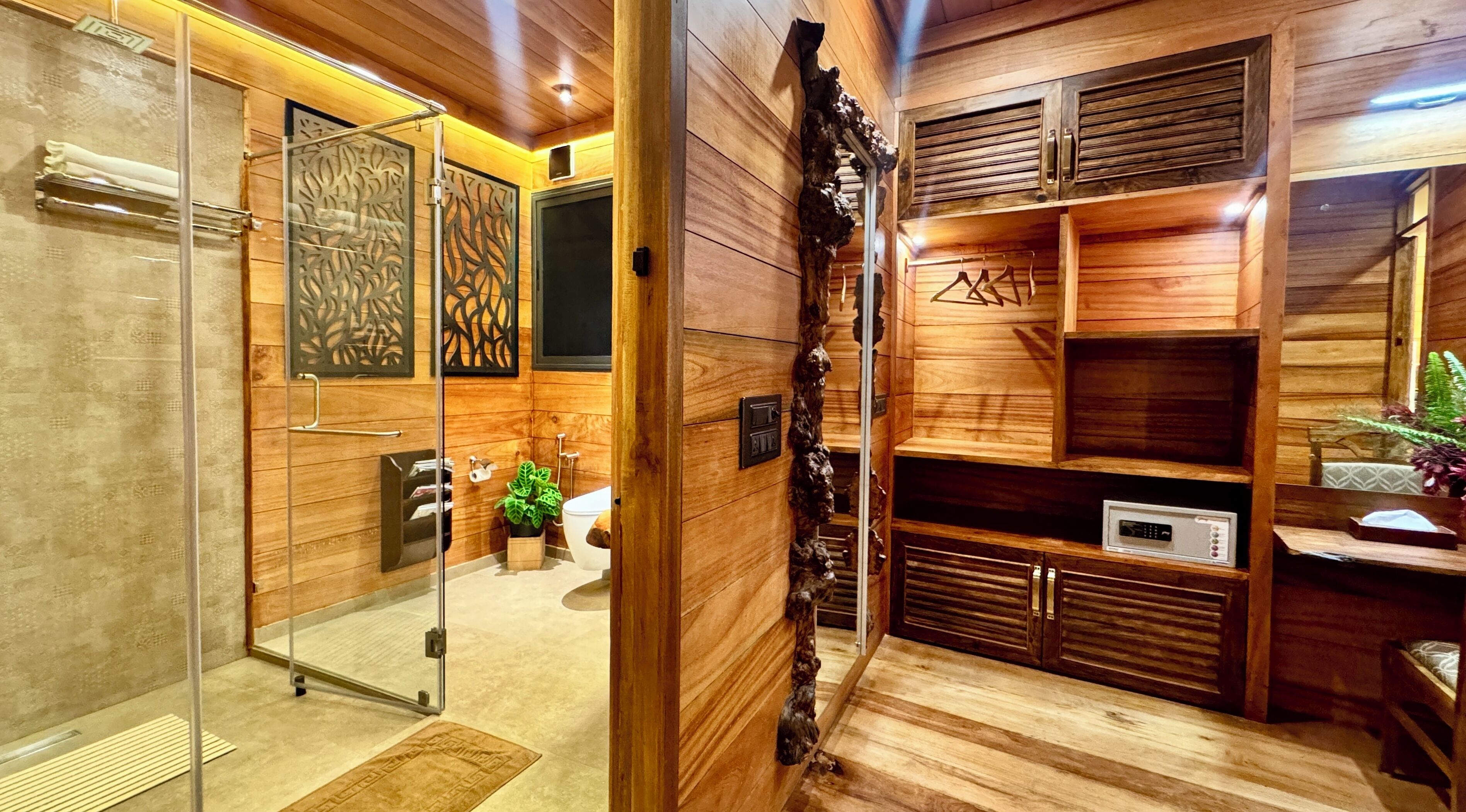 A wooden interior with a glass partition, a sink, a toilet, and a shelf with a plant.