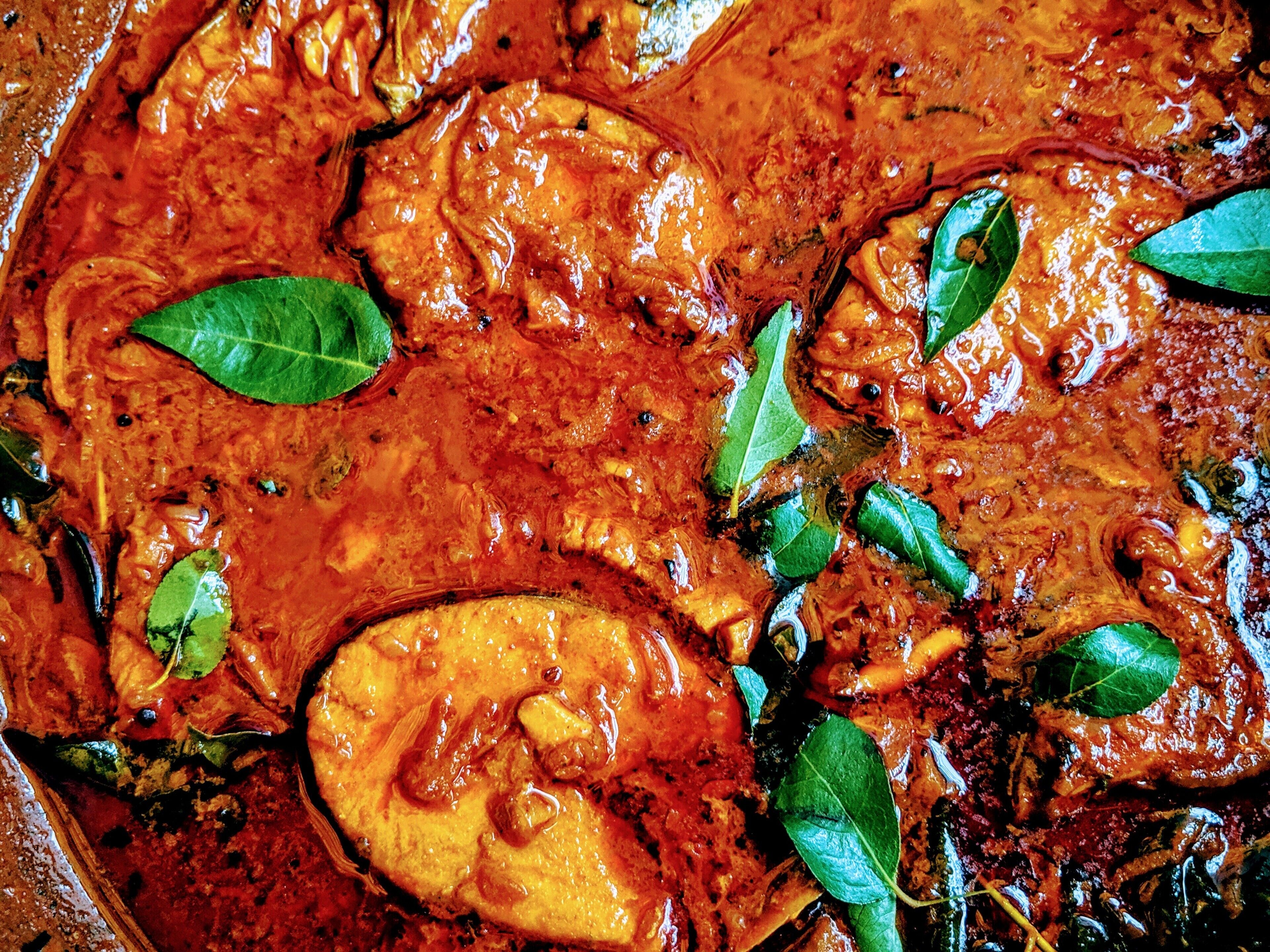 A close-up of a dish with a rich, red sauce and green leaves, likely a curry or stew.